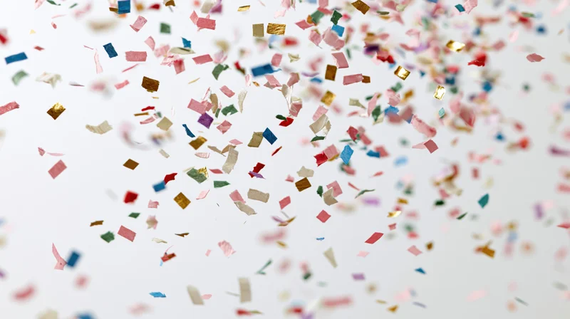 Colorful paper confetti pieces falling and floating mid-air against a white background