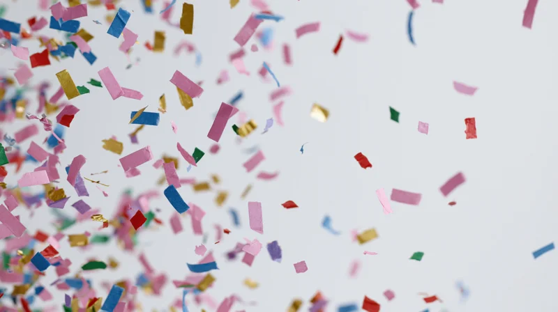 Colorful paper confetti pieces falling and floating mid-air against a white background