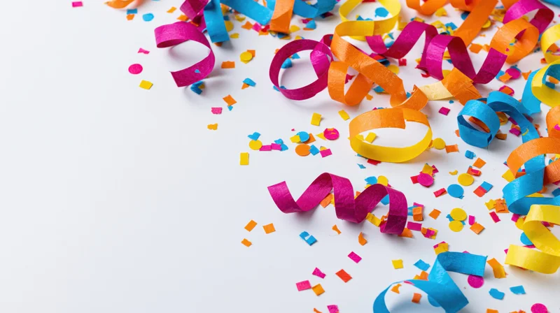 Colorful paper streamers and scattered confetti pieces arranged on white surface with copyspace