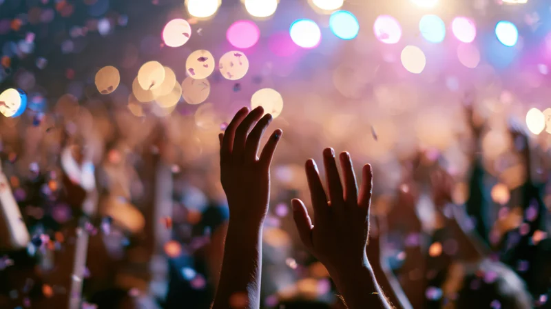 Silhouetted hands raised in a crowd at a concert under colorful stage lights