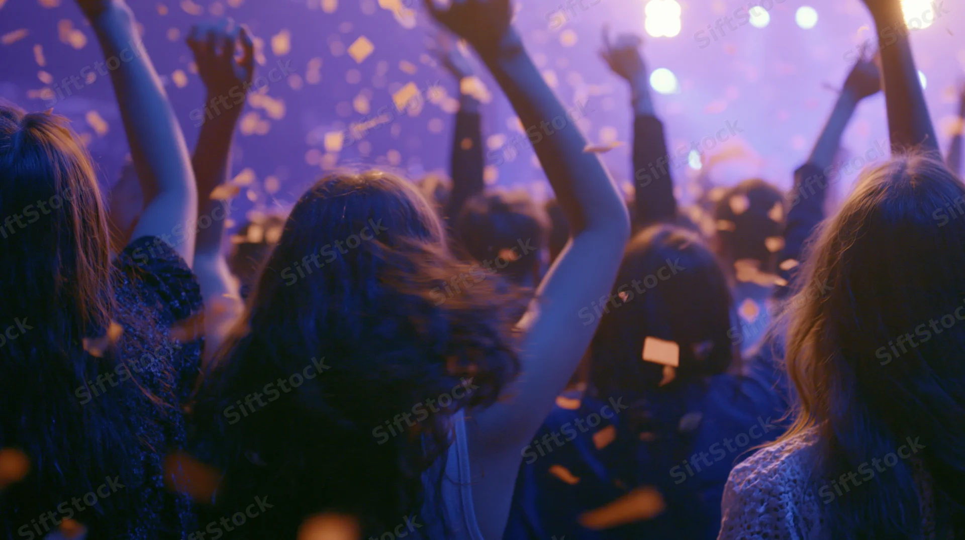 Young people dancing with arms raised at an indoor nightclub concert under purple lights and falling confetti