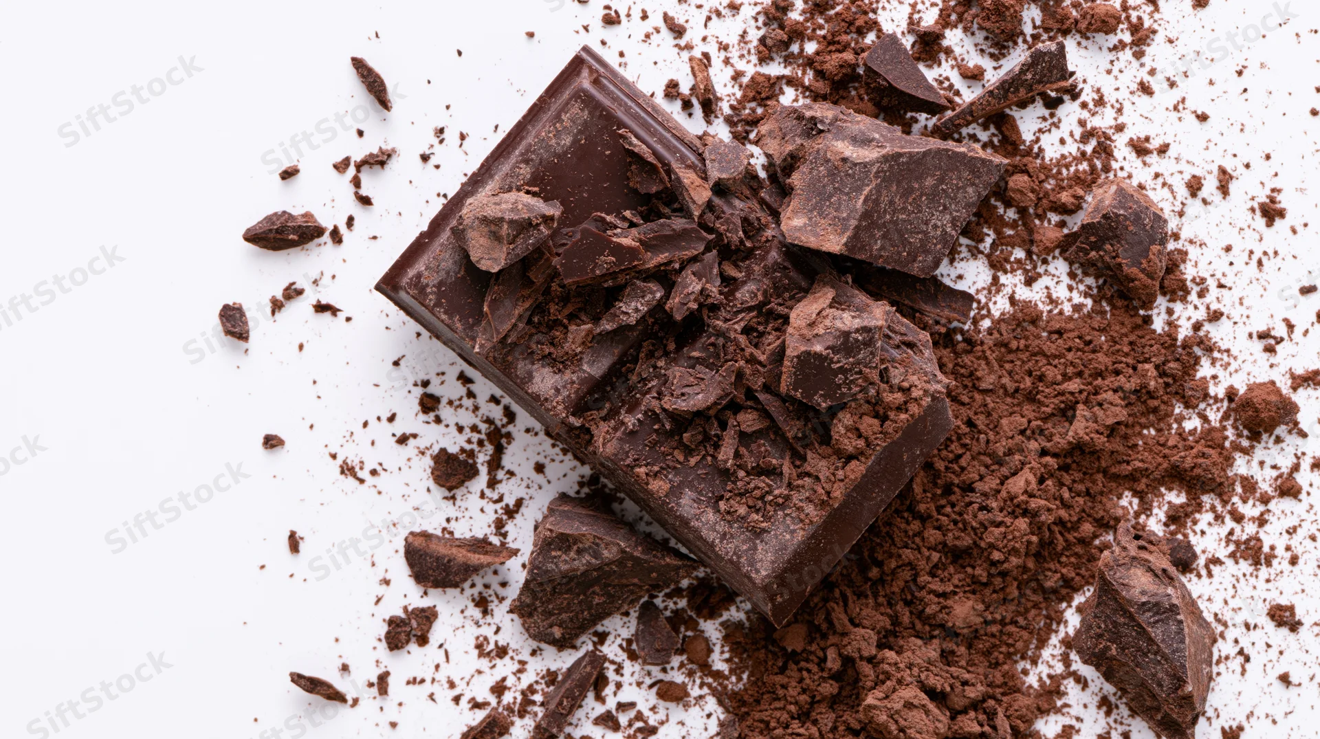 Dark chocolate bar shattered into jagged chunks and powder on white surface