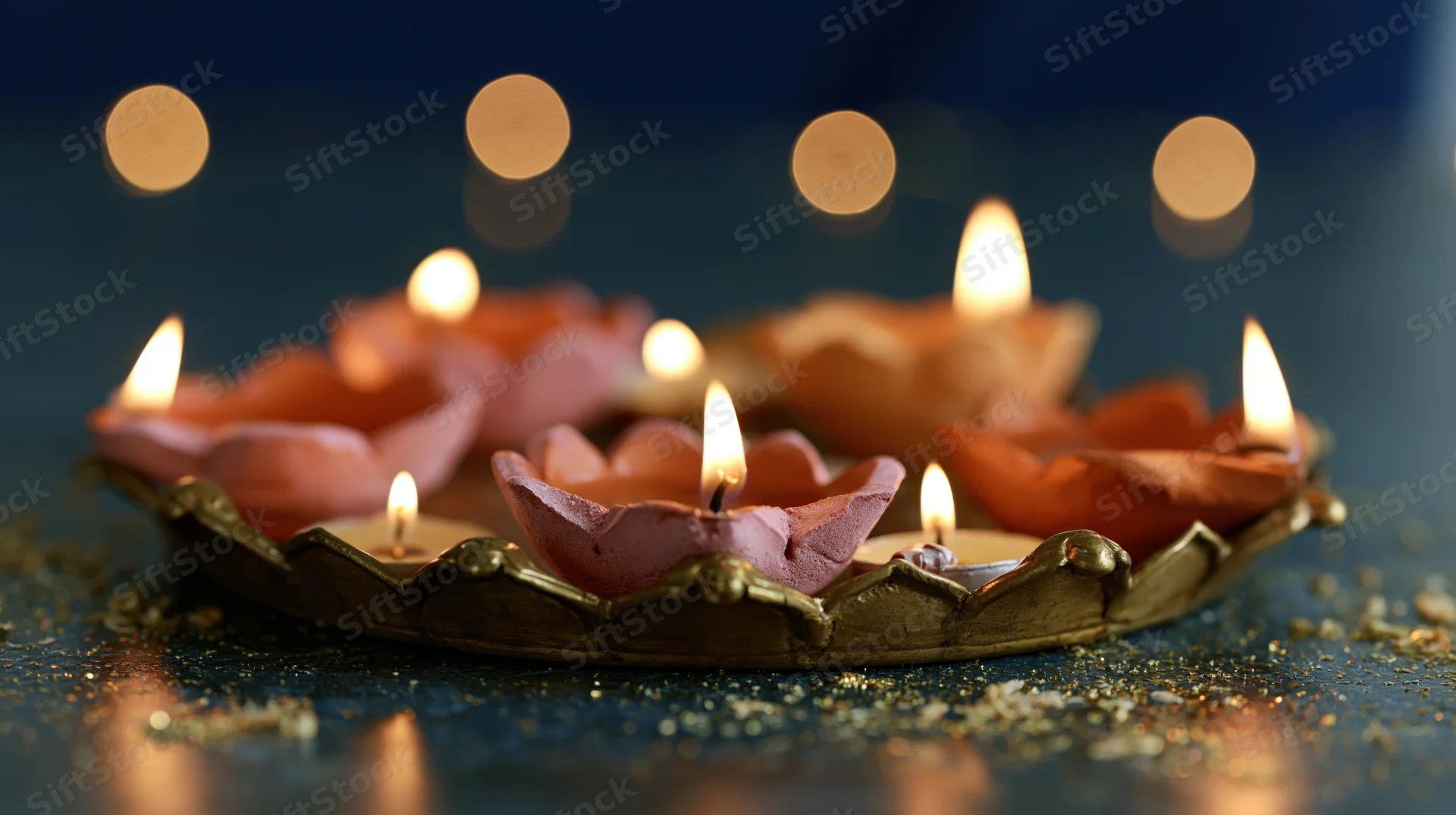Clay diya oil lamps shaped like lotus flowers lit on a decorative tray with glitter and bokeh lights in the background