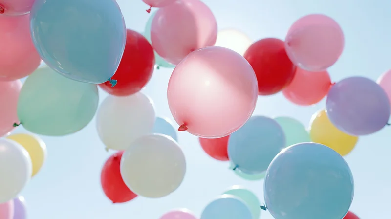 Colorful helium balloons floating upward against a clear blue sky