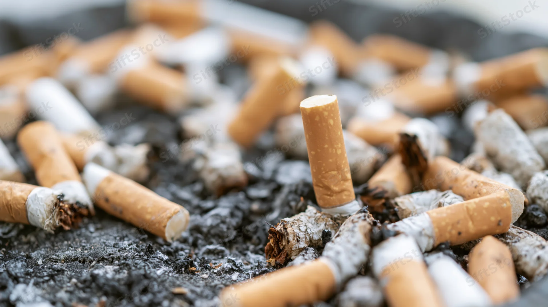 Closeup of cigarette butts and ash scattered on a dark surface