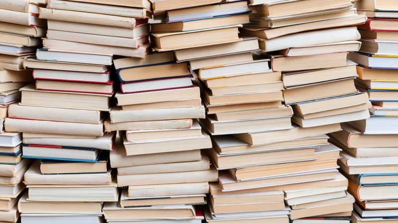 Stacks of hardcover and paperback books piled irregularly in a dense arrangement