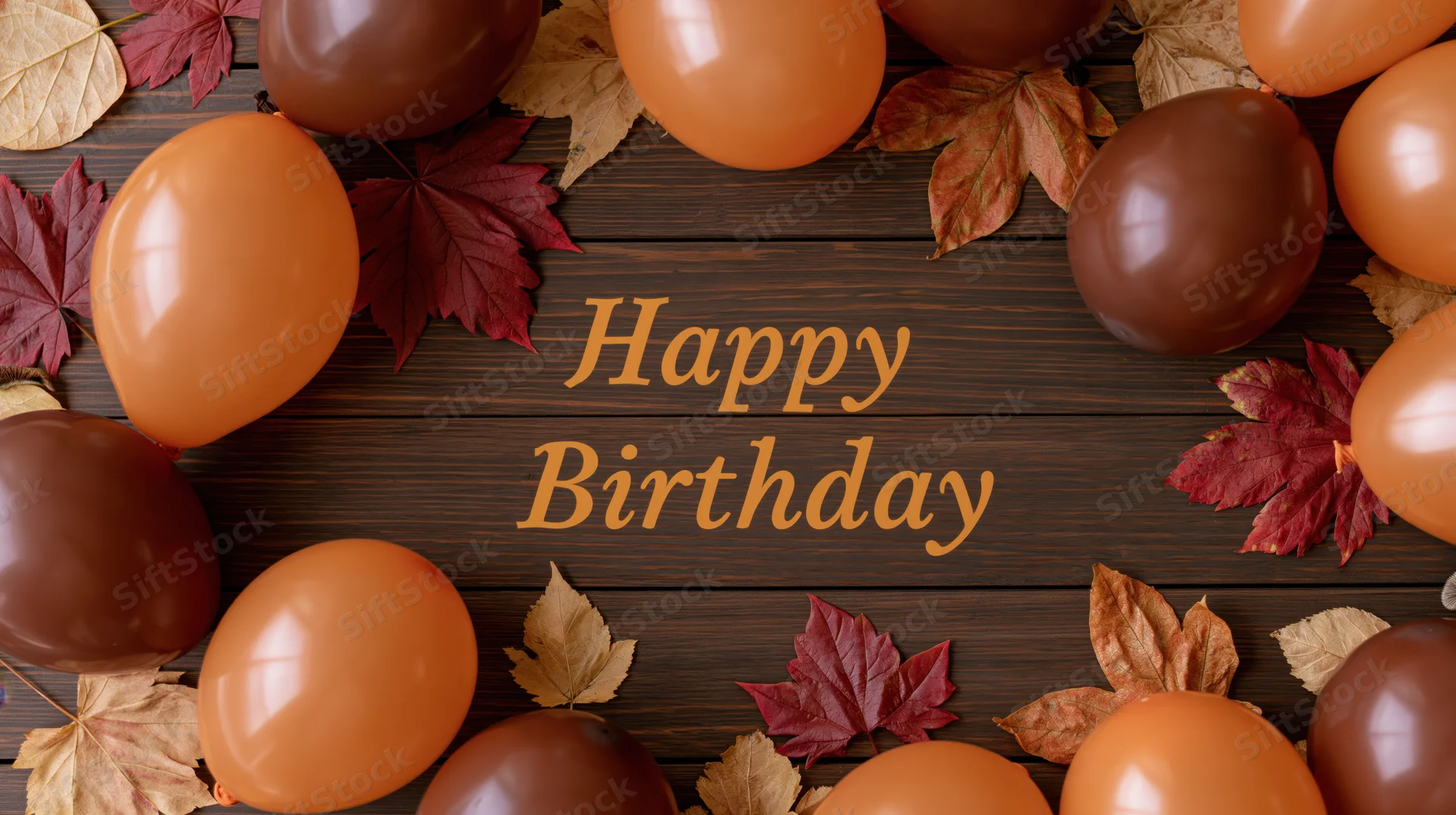 Orange and brown balloons with autumn leaves arranged on wooden surface framing happy birthday text