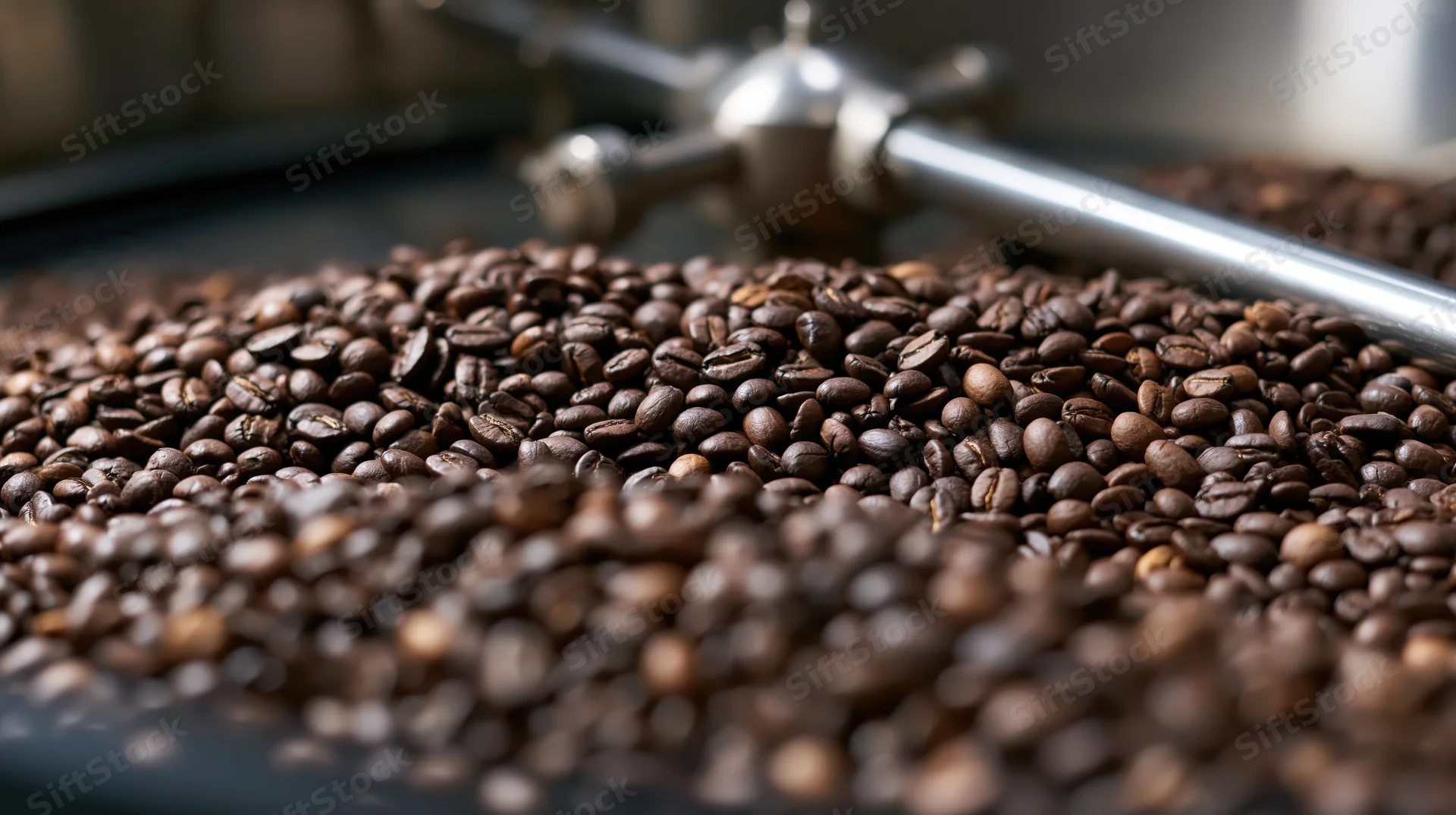 Roasted coffee beans spread across industrial cooling tray with metal machinery in background