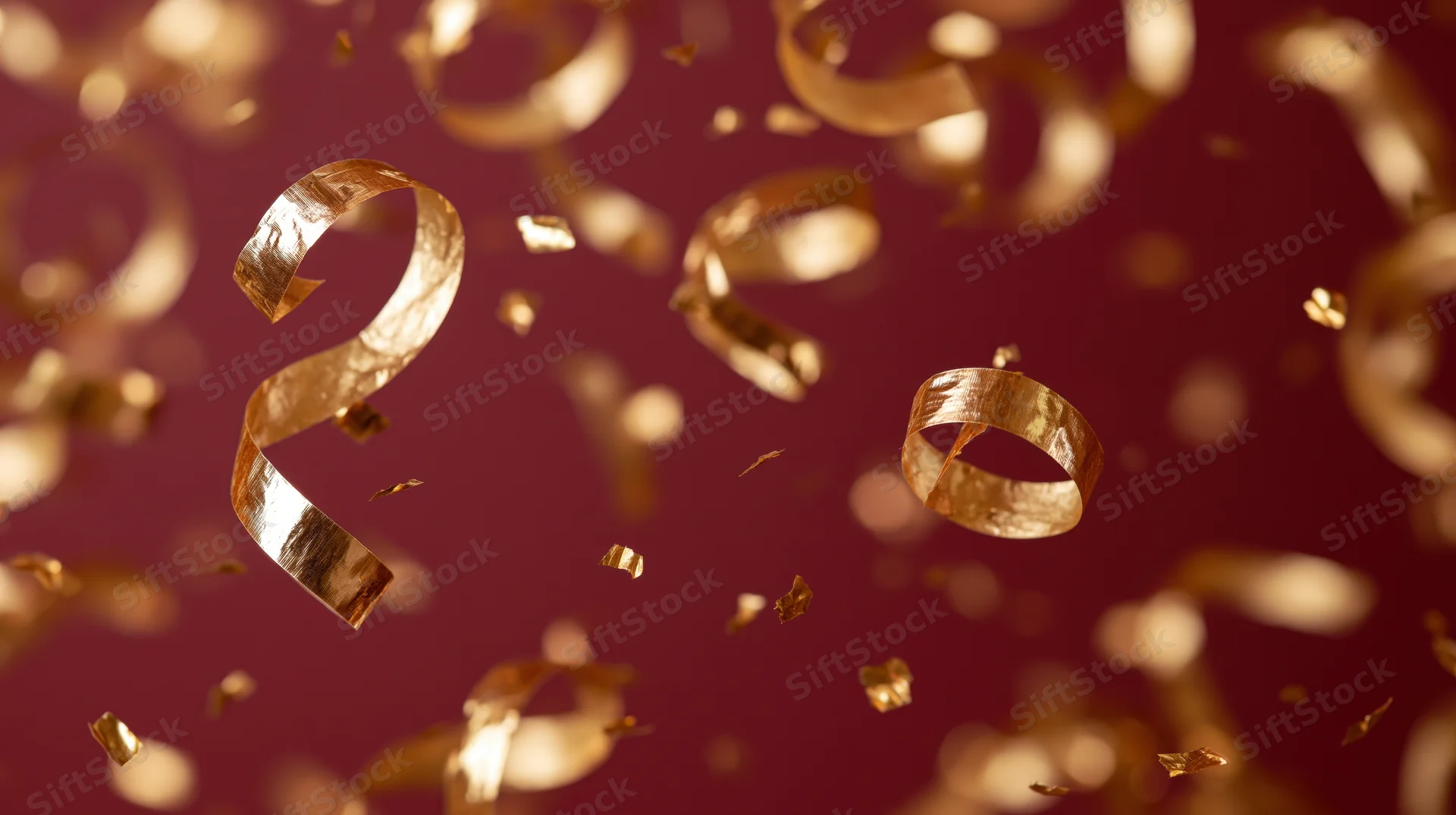 Gold metallic ribbon confetti falling against a red background