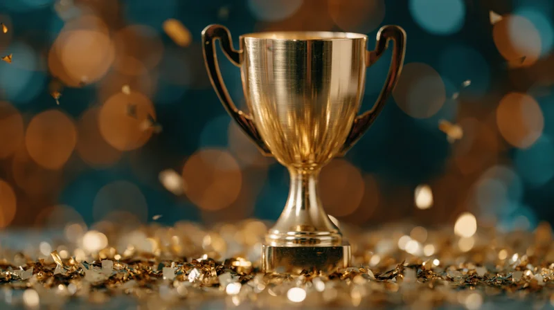Gold trophy cup standing on glittery surface with confetti and bokeh lights in background