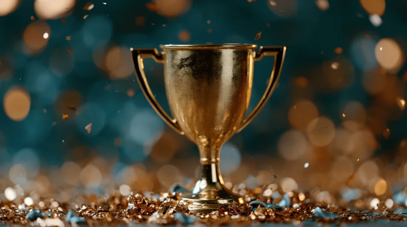 Gold trophy cup standing on a glitter-covered surface with bokeh lights in the background