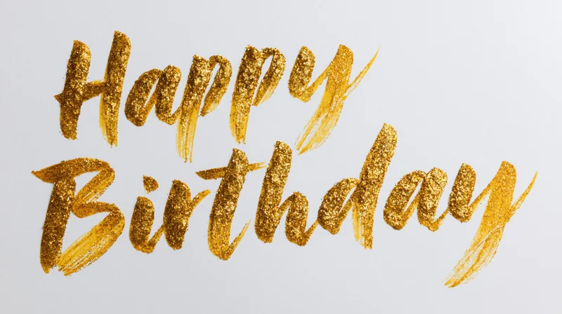 Hand-lettered happy birthday text in gold glitter brushstroke calligraphy on white background