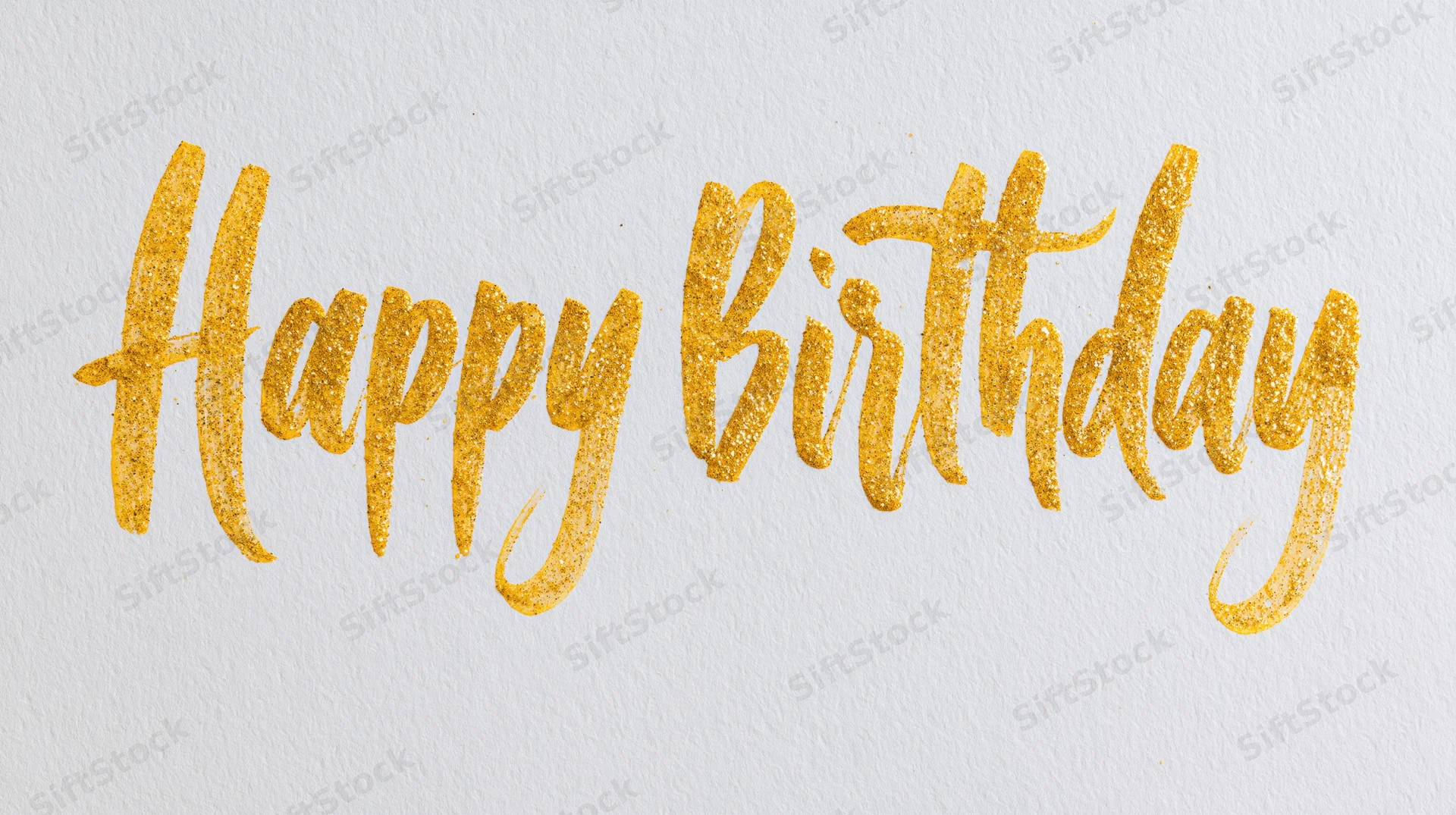 Hand-lettered happy birthday calligraphy in gold glitter on white textured paper