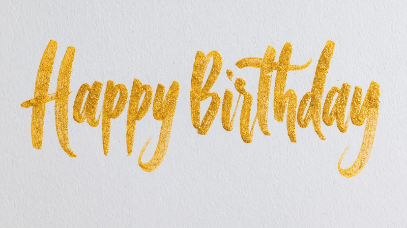 Hand-lettered happy birthday calligraphy in gold glitter on white textured paper