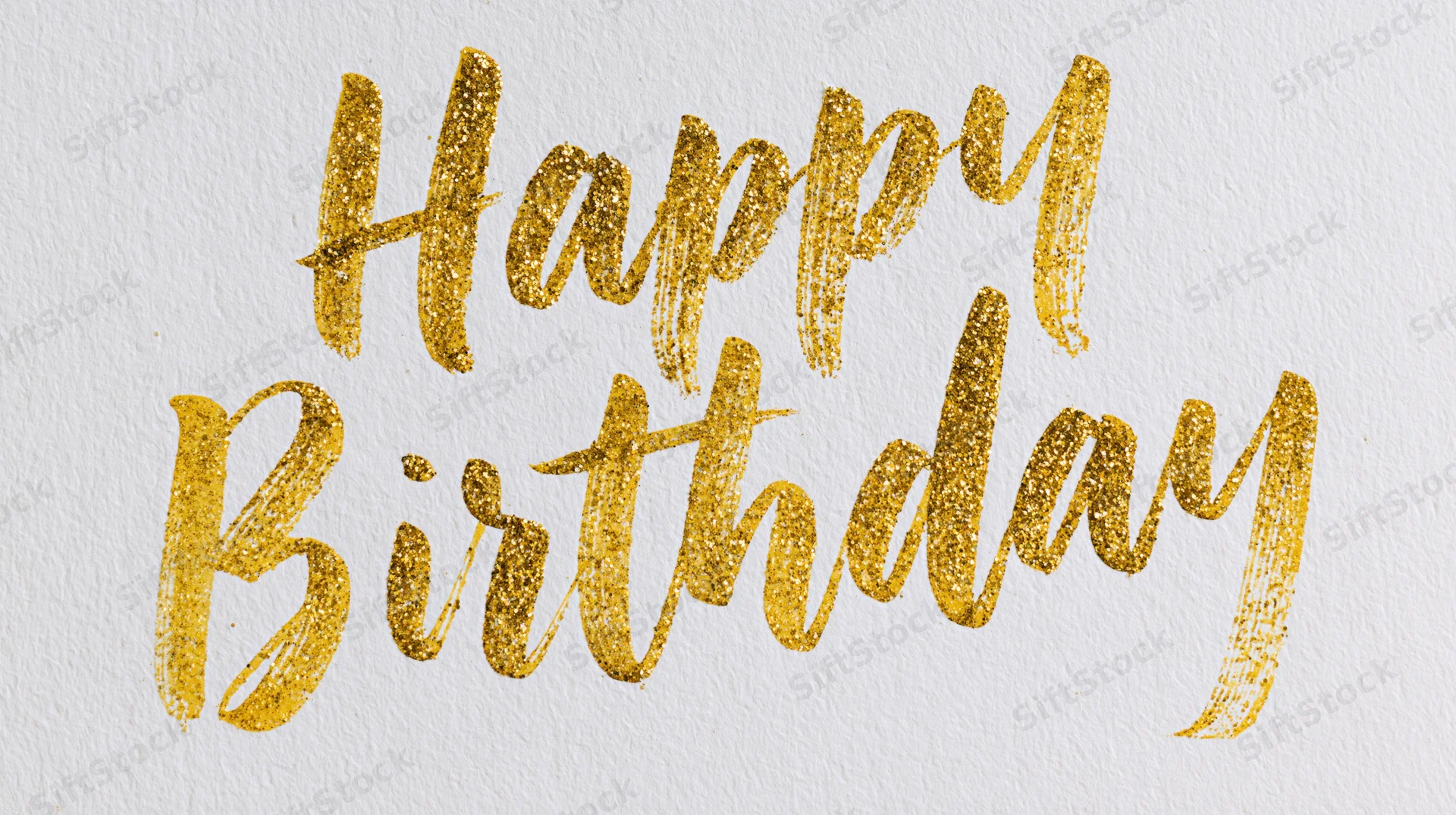Hand-lettered happy birthday calligraphy in gold glitter on textured white paper