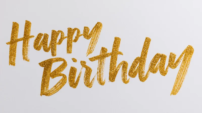 Hand-lettered happy birthday text in gold brushstroke calligraphy on white background