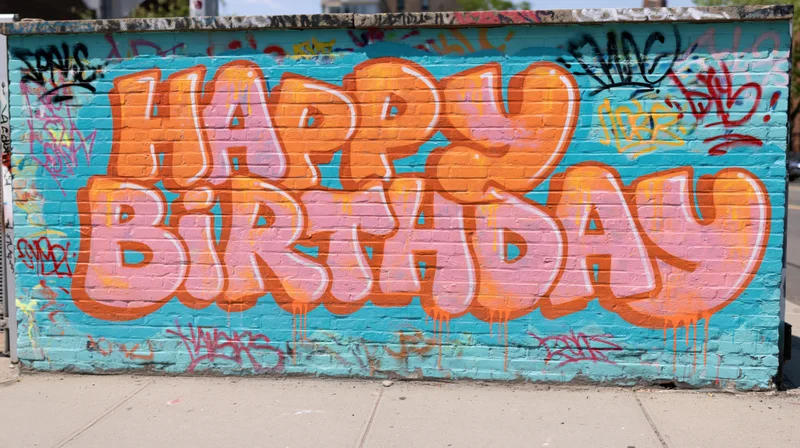 Happy birthday graffiti lettering spray-painted on a brick wall in an urban outdoor setting