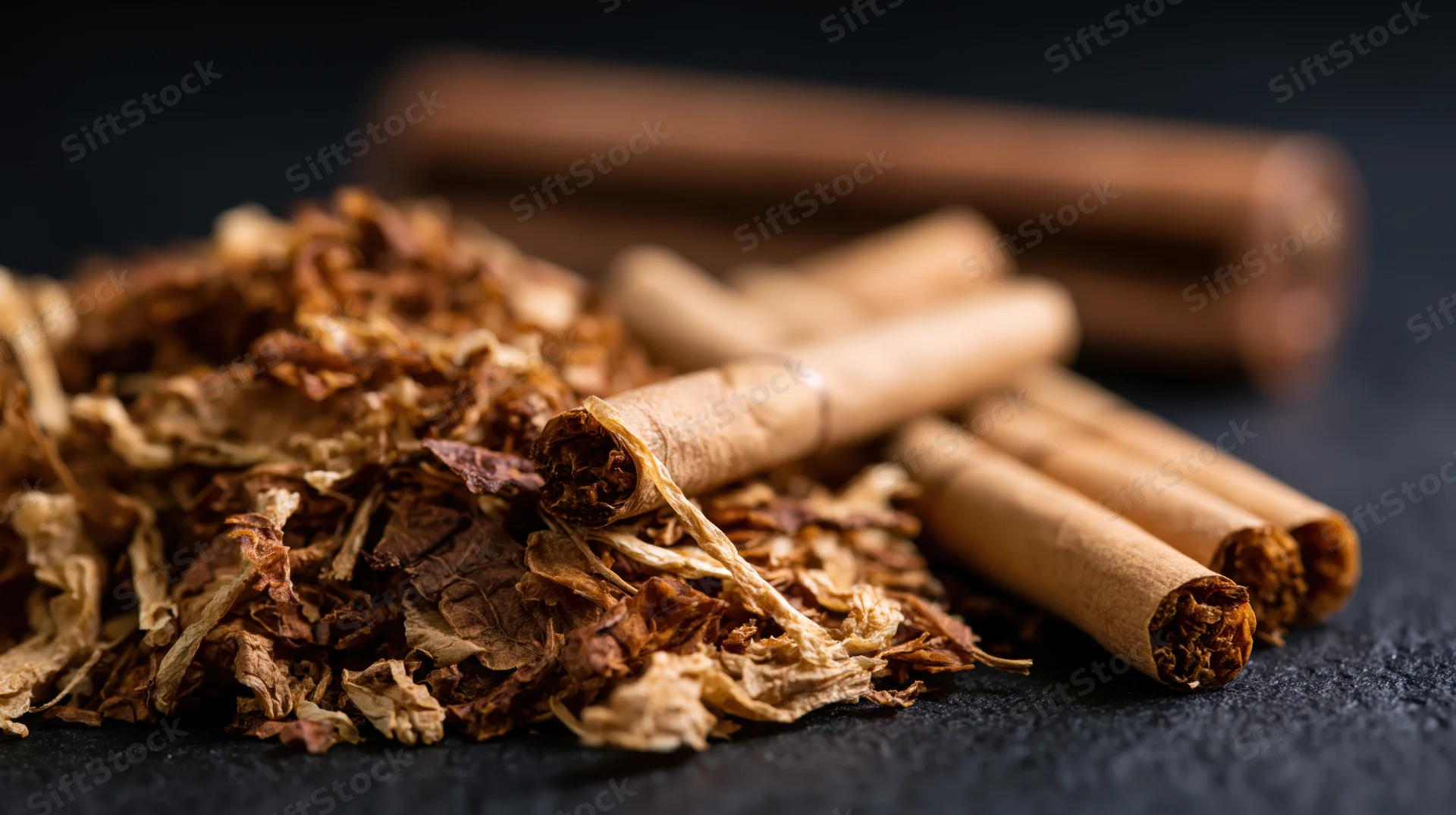 Loose shredded tobacco piled beside rolled cigarettes on a dark surface