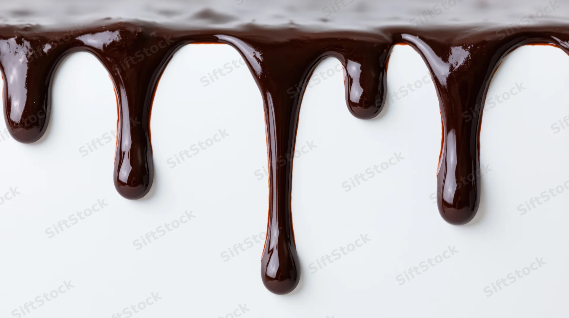 Melted dark chocolate dripping downward along the top edge of a white surface