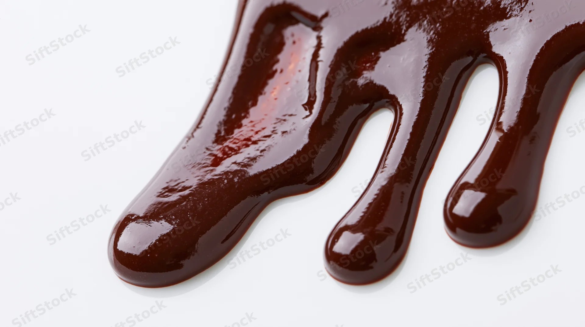 Melted dark chocolate dripping in slow flowing streams on white background