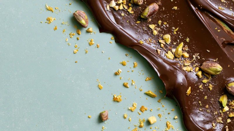 Melted dark chocolate spread with pistachios on a sage green surface