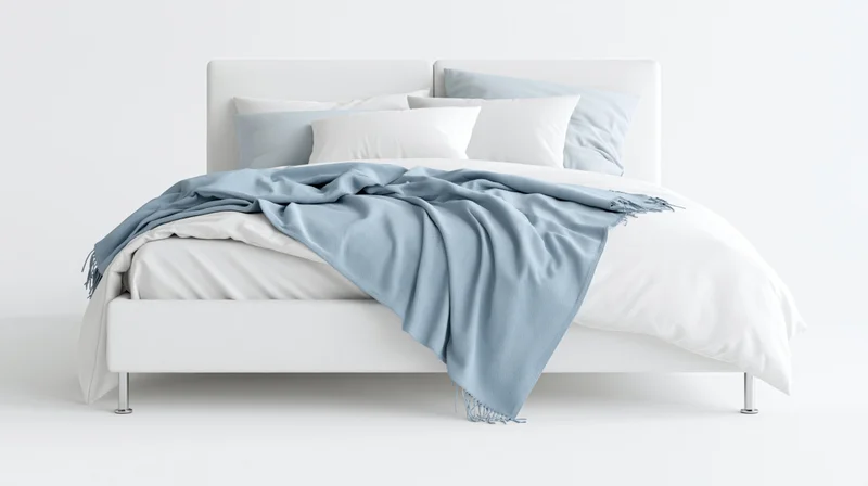 Modern double bed with white upholstered frame and chrome legs, covered in white bedding and blue blanket, in a minimalist white room