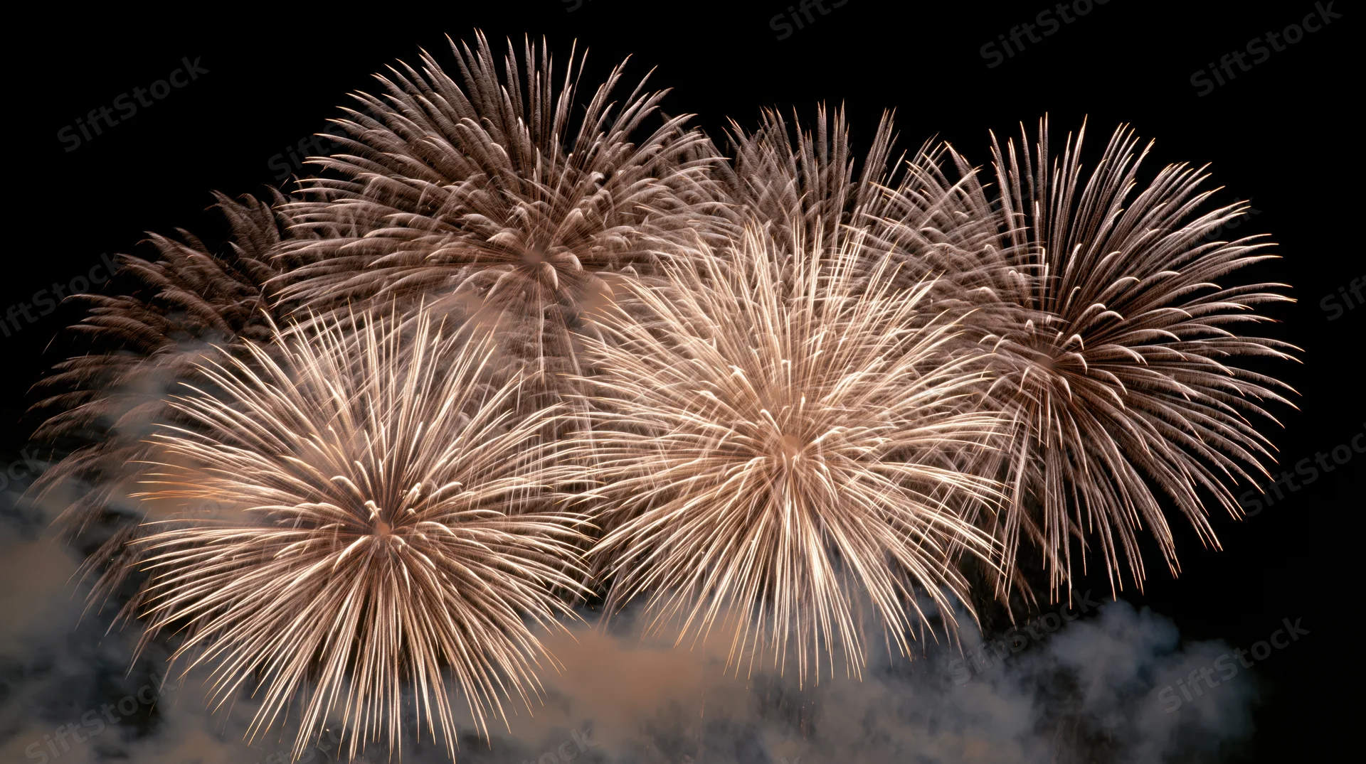Multiple fireworks bursting simultaneously against a black sky with smoke trails