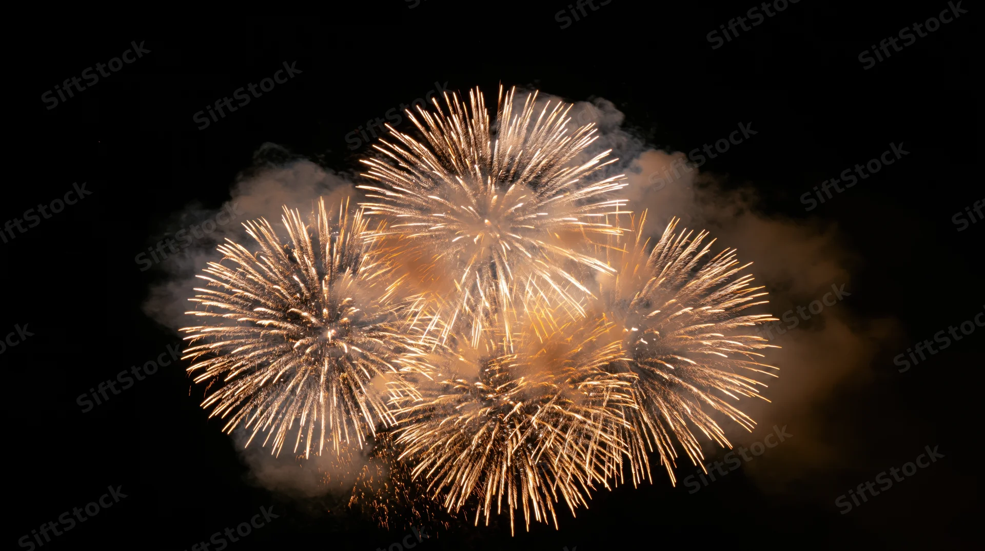 Multiple fireworks bursting simultaneously in the night sky with smoke trails