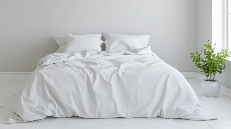 Unmade white cotton duvet bed with four pillows in minimalist bedroom near window with potted plant