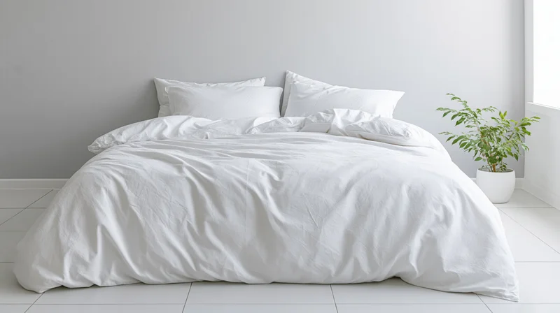 White cotton duvet and four pillows on a bed in a minimalist bedroom with a potted plant beside the window