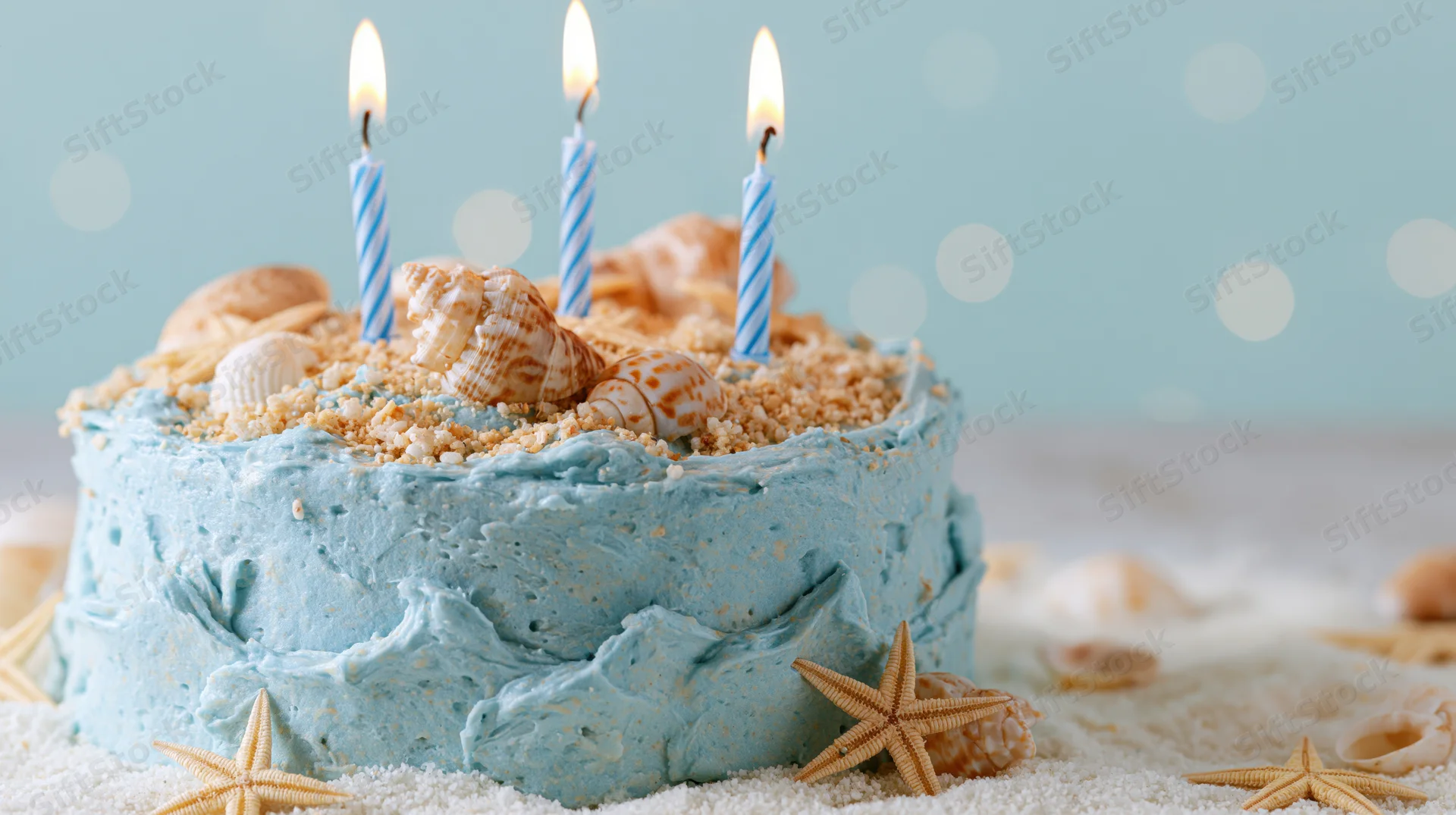 Ocean-themed birthday cake with blue frosting, seashells and starfish on sand, lit candles on top