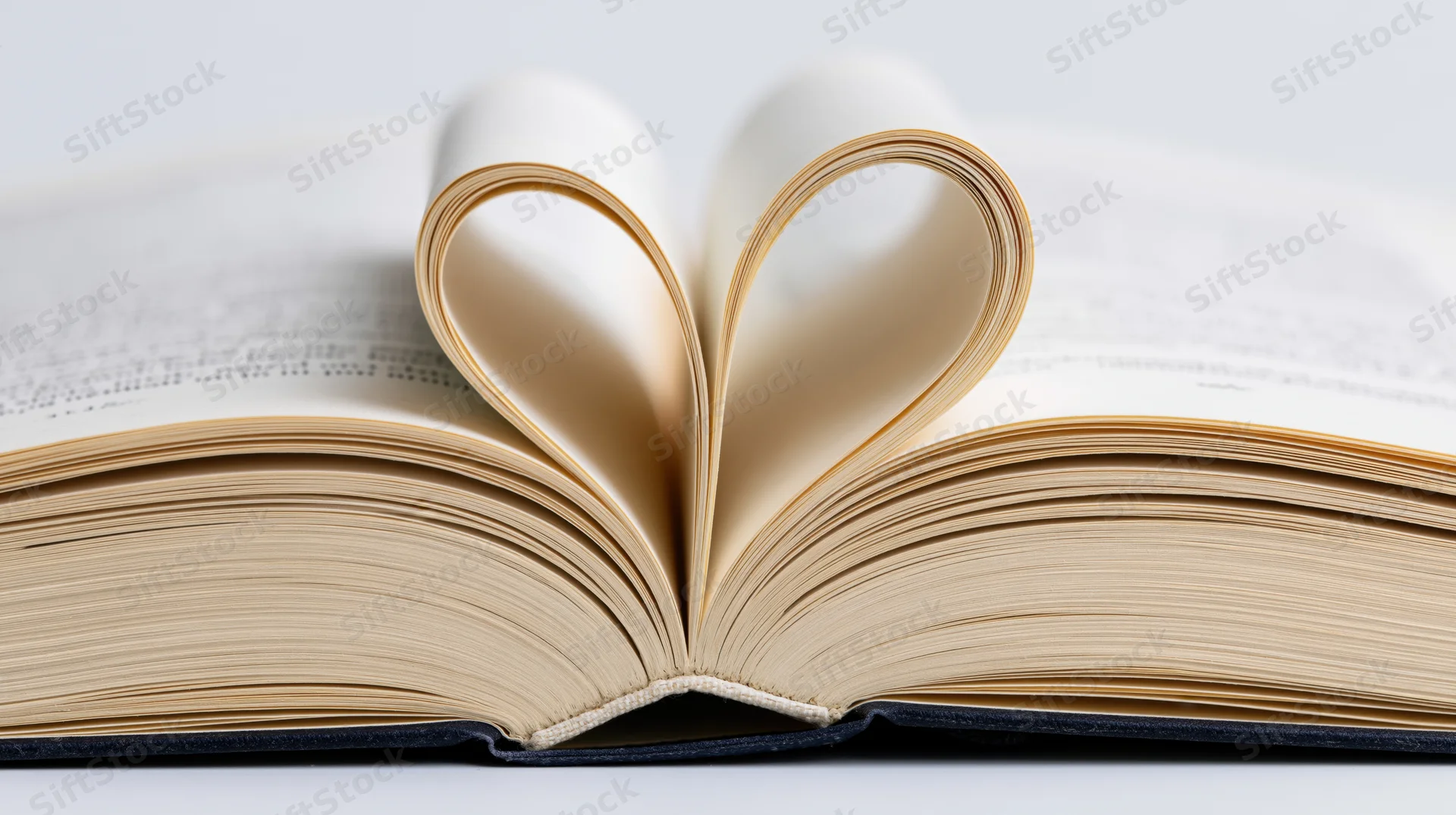 Open hardcover book with pages folded into heart shape lying flat on white surface