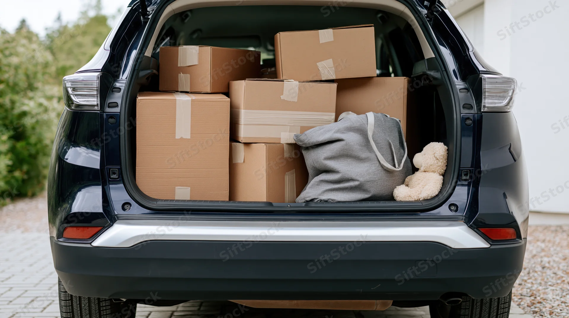 Open trunk of dark navy suv filled with cardboard boxes and household items in driveway