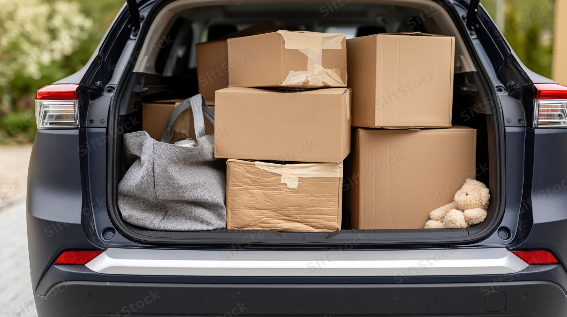 Open trunk of a dark navy suv filled with cardboard boxes and a teddy bear, ready for moving