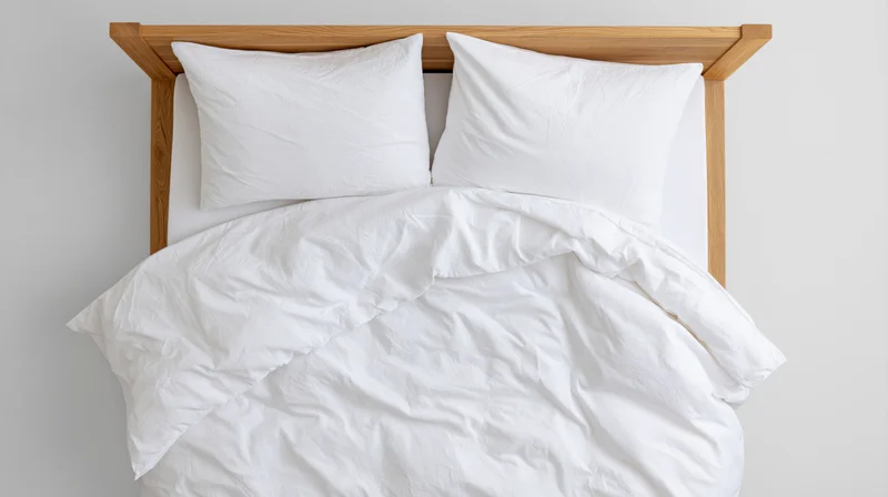 Overhead view of a double bed with white bedding and wooden headboard in a minimalist bedroom