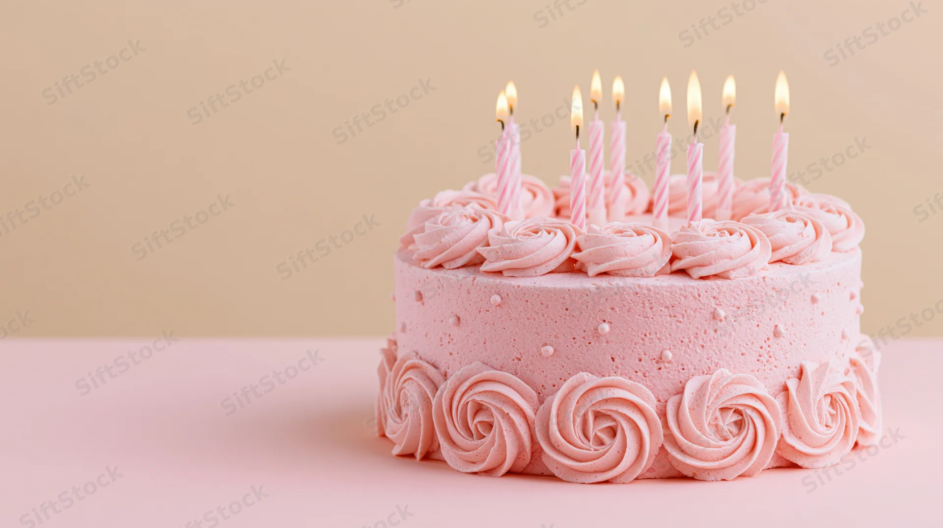 Pink birthday cake with eight lit striped candles and piped rosettes on a pastel surface