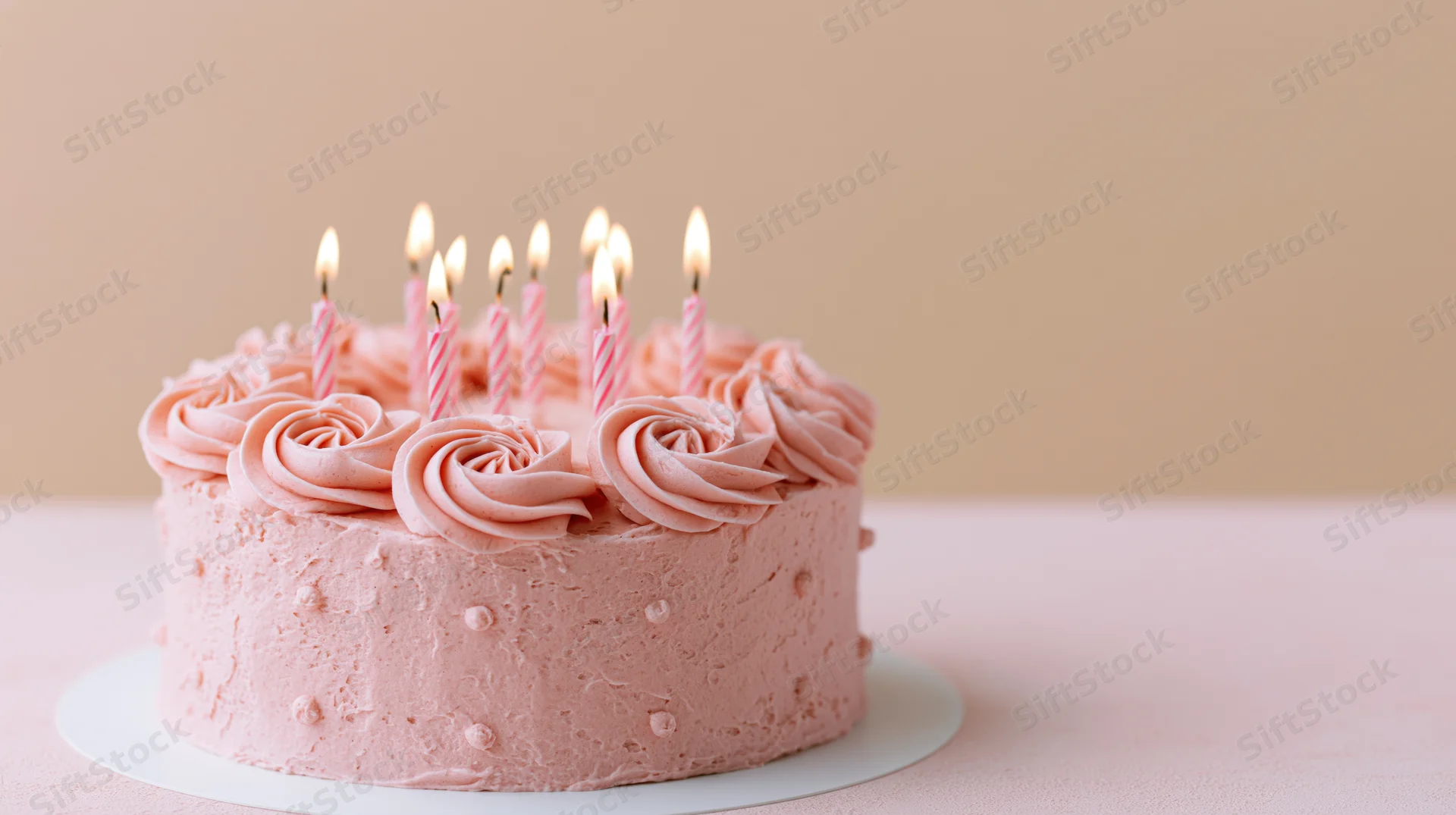 Pink birthday cake with lit striped candles and piped rosettes on a cake stand