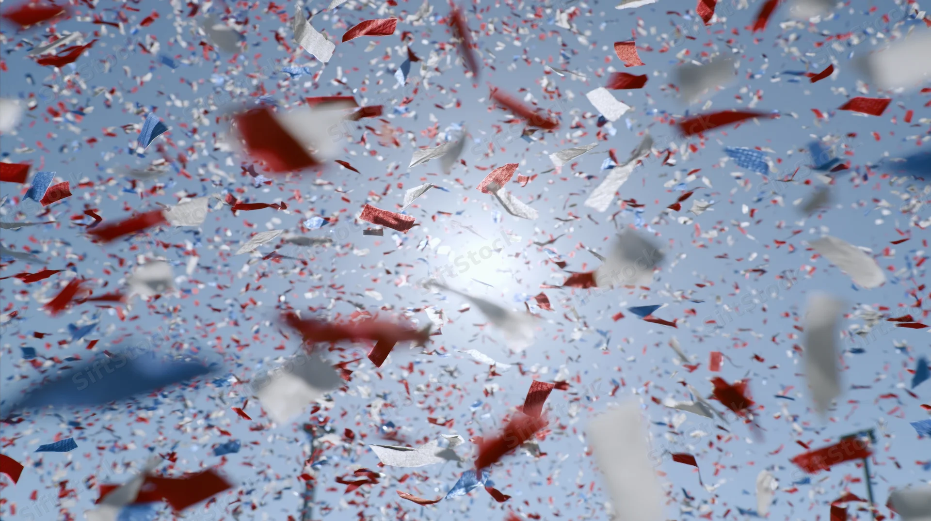 Red white and blue paper confetti falling against a bright sky during a festive outdoor celebration
