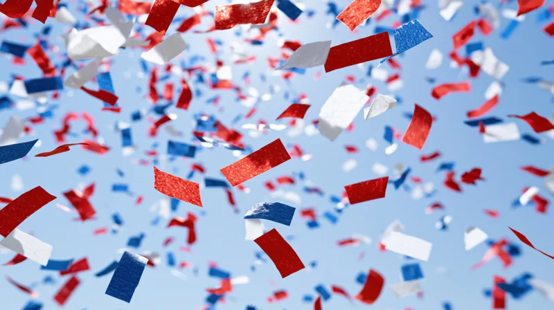 Red white and blue paper confetti falling against a clear blue sky
