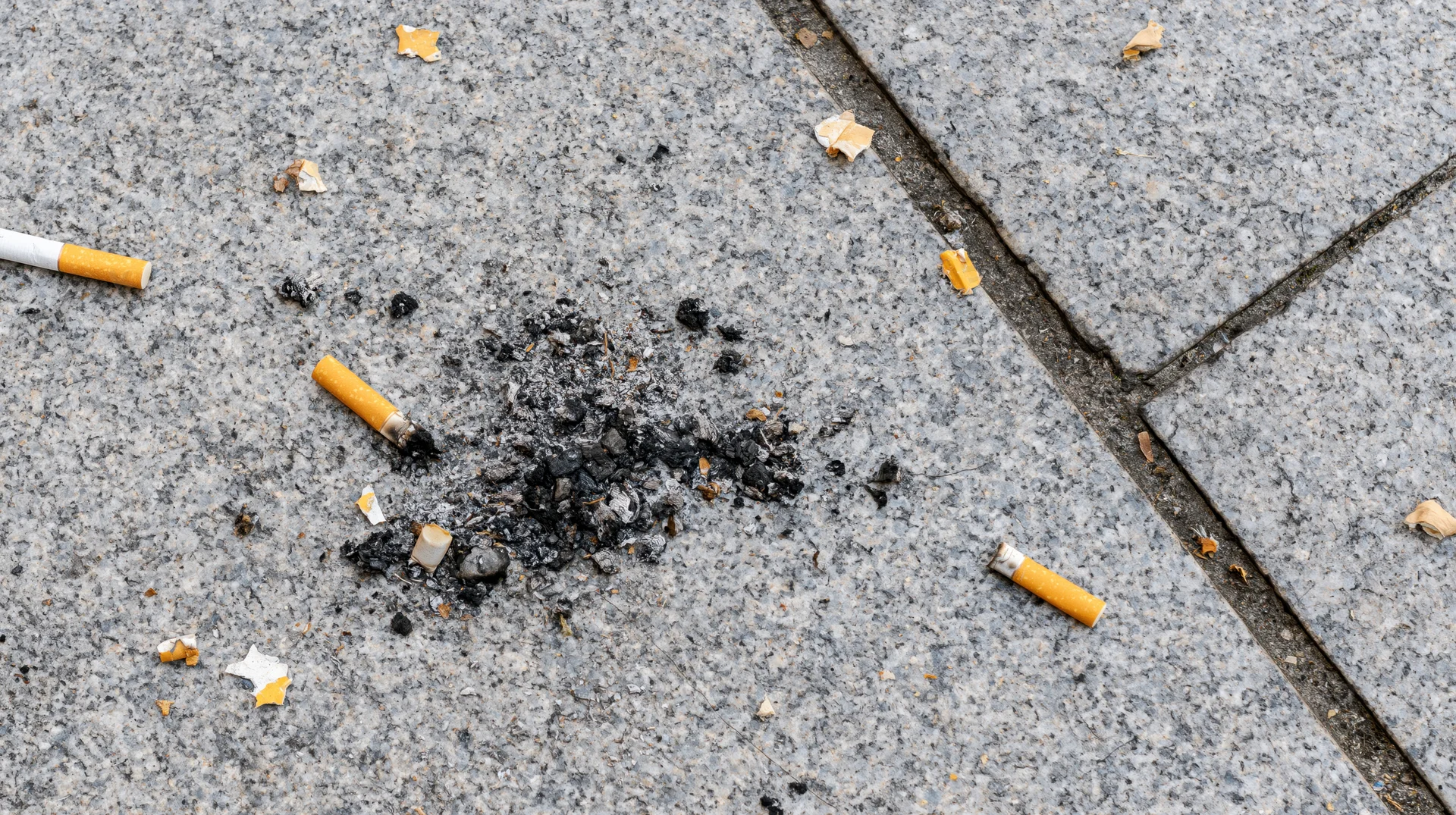 Cigarette butts and ash scattered on cracked concrete sidewalk