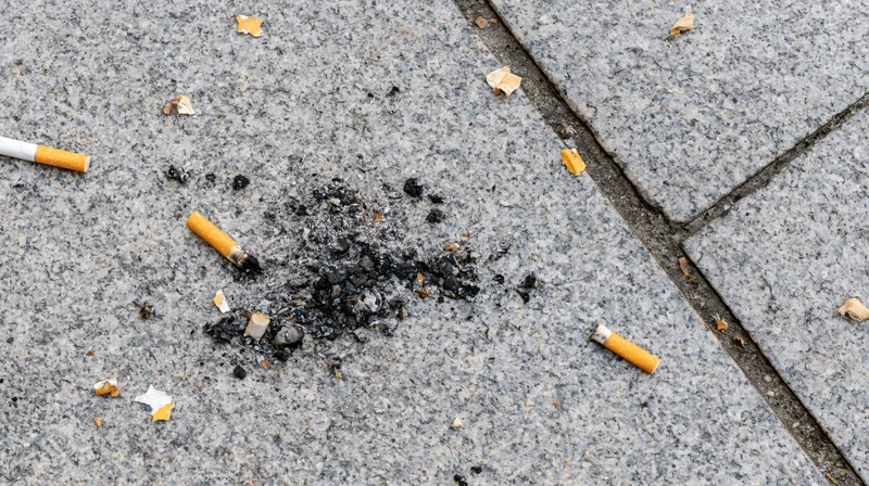 Cigarette butts and ash scattered on cracked concrete sidewalk