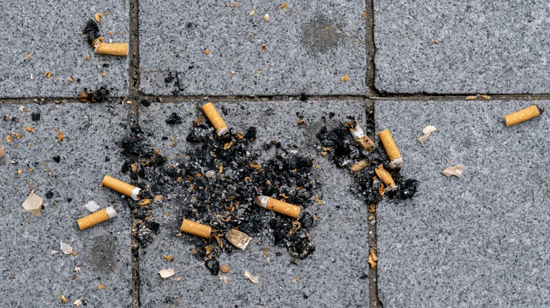 Cigarette butts and ash scattered on cracked concrete pavement