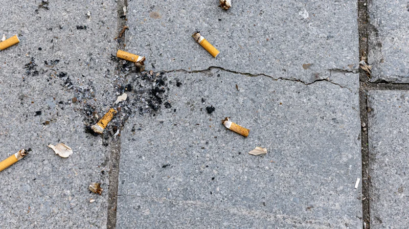Cigarette butts and ash scattered on cracked concrete sidewalk
