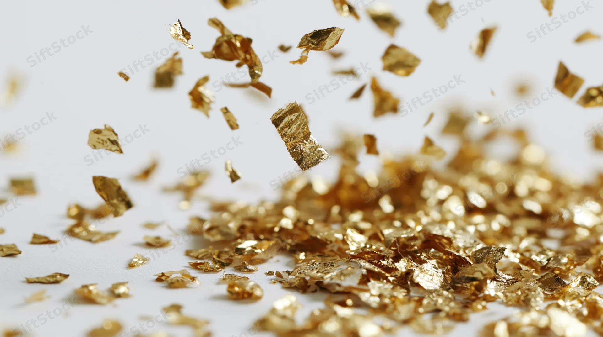 Gold metallic confetti pieces falling and tumbling midair over white surface