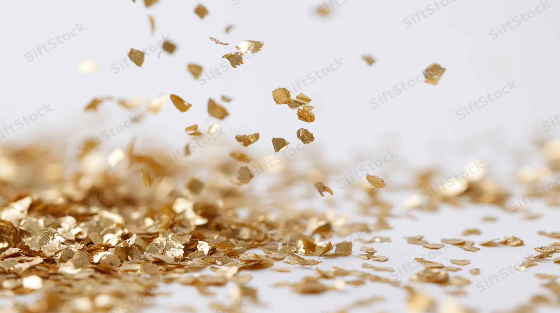 Gold metallic confetti pieces falling and tumbling midair over a white surface