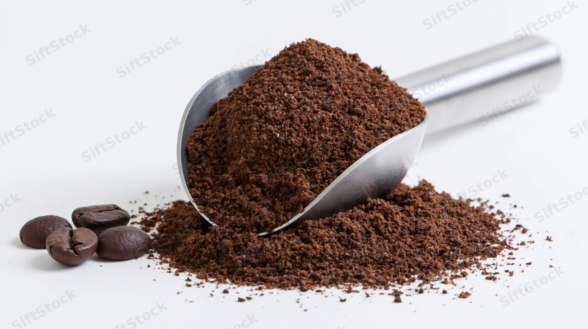 Stainless steel scoop filled with coarse ground coffee resting on a pile with whole beans beside it on white surface