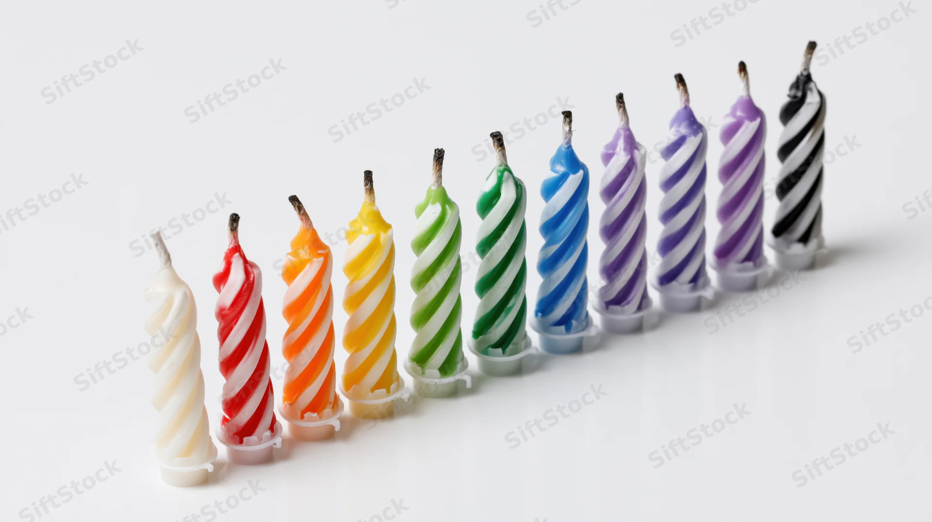 Ten unlit spiral-striped birthday candles arranged in a row on a white surface