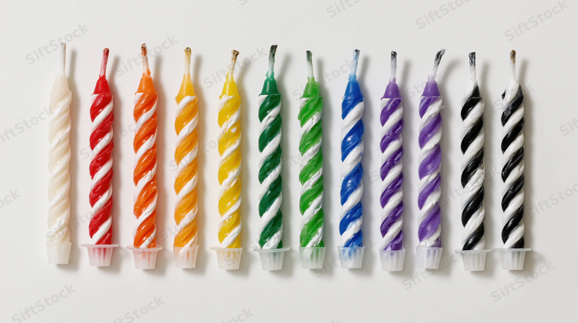 Ten unlit birthday candles with spiral stripes arranged in a row on white background