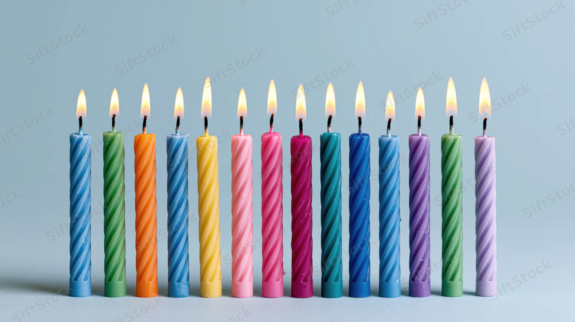 Twelve lit colorful spiral candles arranged in a row on a light blue surface