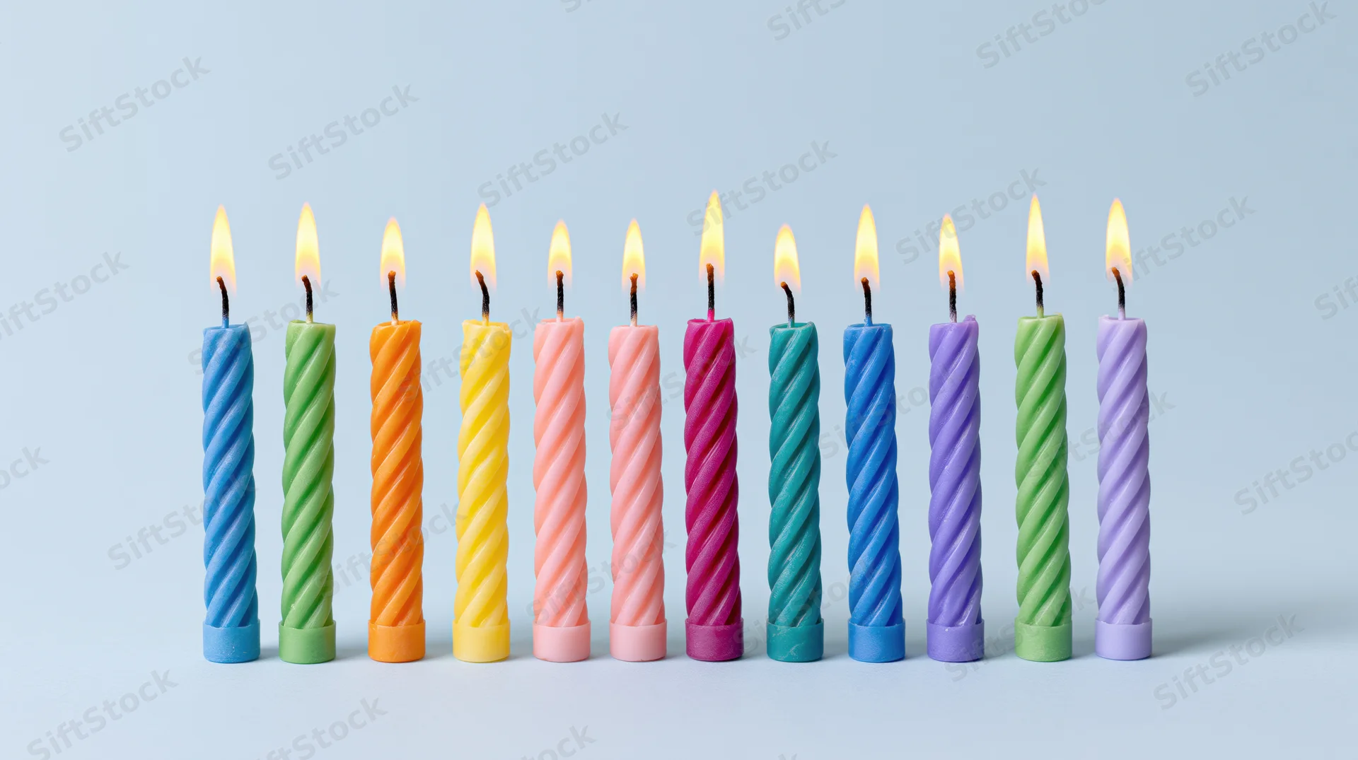Twelve lit colorful spiral candles arranged in a row on a light background